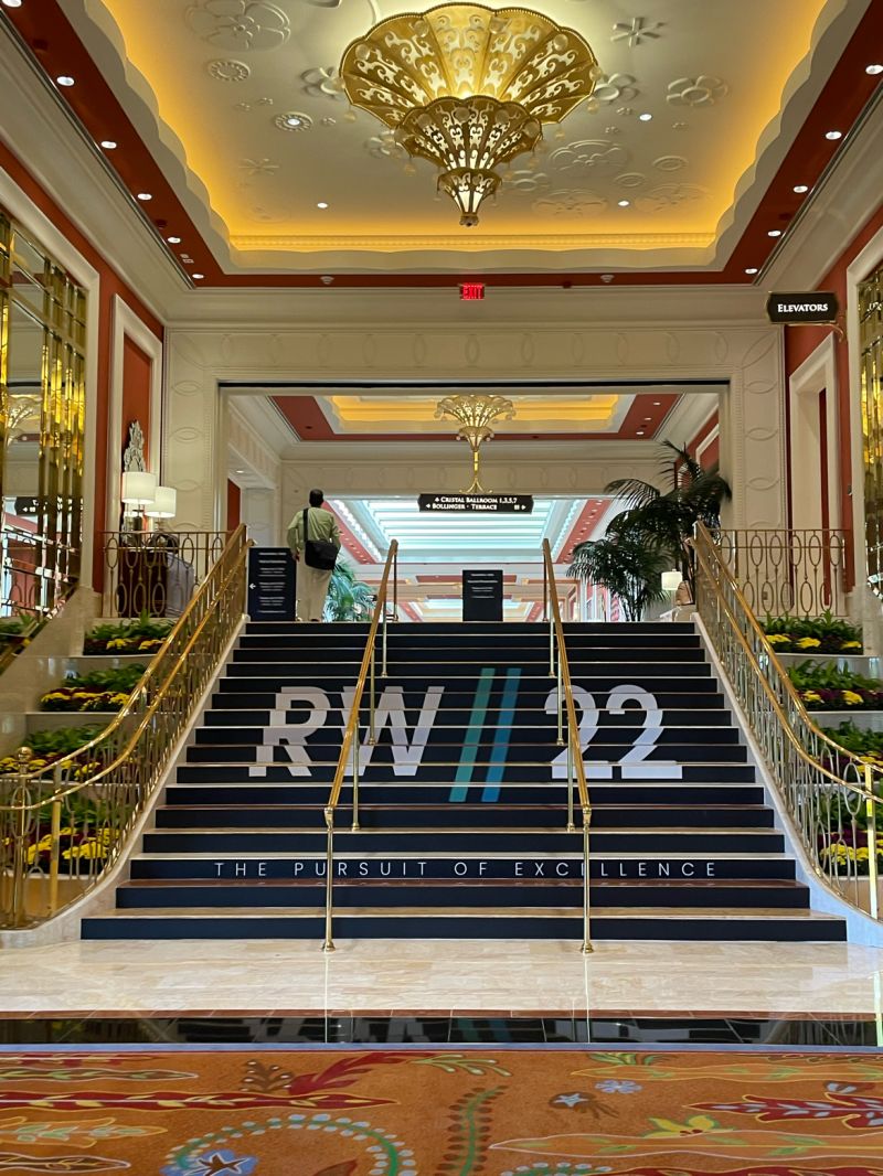 Elegant staircase with the text 'RW//22 THE PURSUIT OF EXCELLENCE' in a luxurious lobby setting.