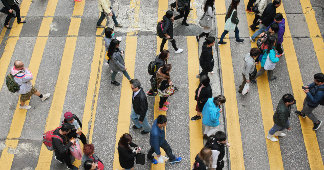 Aerial view of diverse pedestrians crossing a street with yellow painted lines.