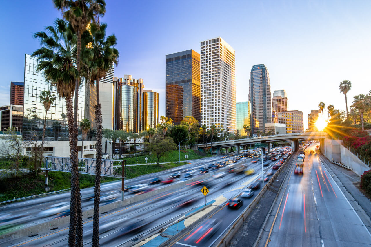 Urban skyline with palm trees alongside a busy highway during sunset in a city.