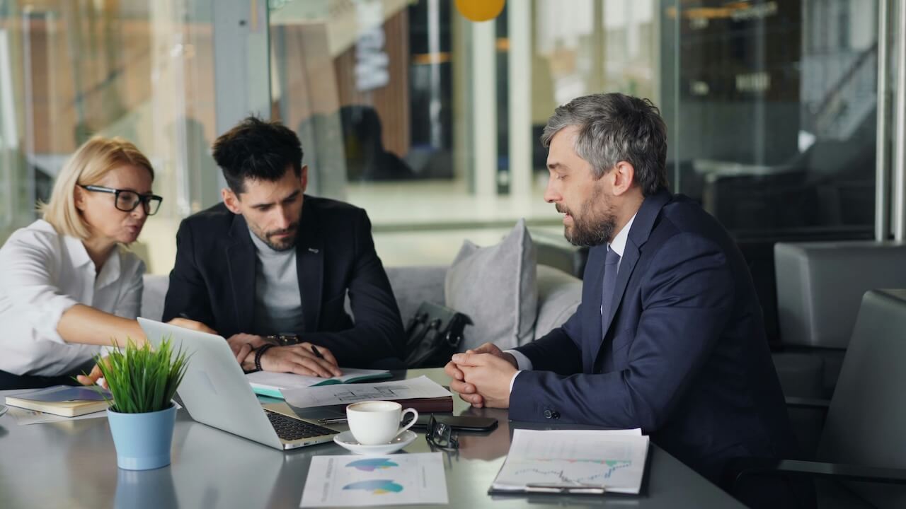 Three professionals engaged in a meeting, discussing documents and a laptop on a conference table.