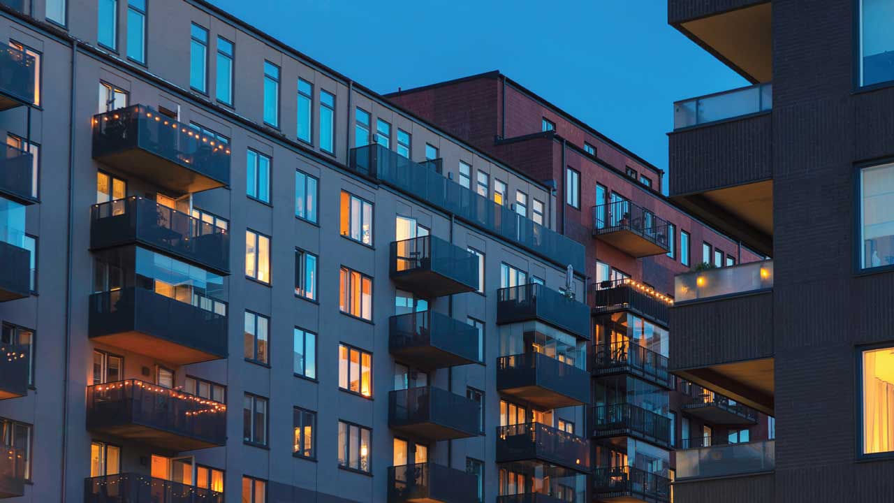 Modern apartment buildings with balconies, illuminated windows, and a twilight sky.