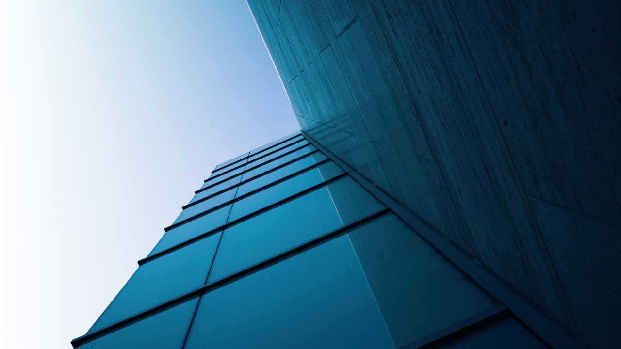 Low-angle view of a modern glass building with a blue and gray facade under a clear sky.