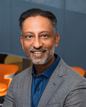 Professional portrait of a man with a grey beard, wearing a blazer and blue shirt, smiling.