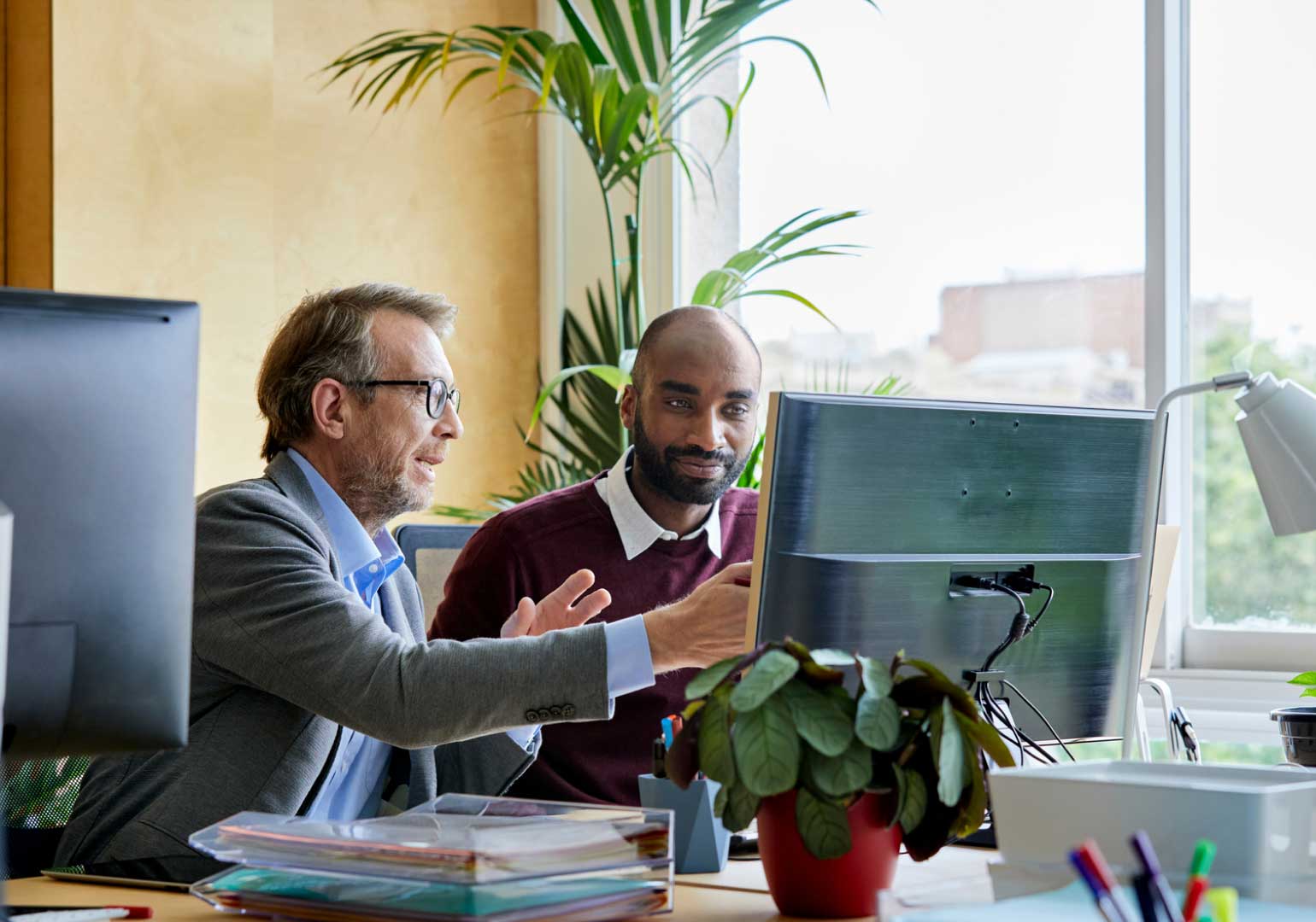 Two colleagues collaborate at a desk, discussing insights while focused on a computer screen.