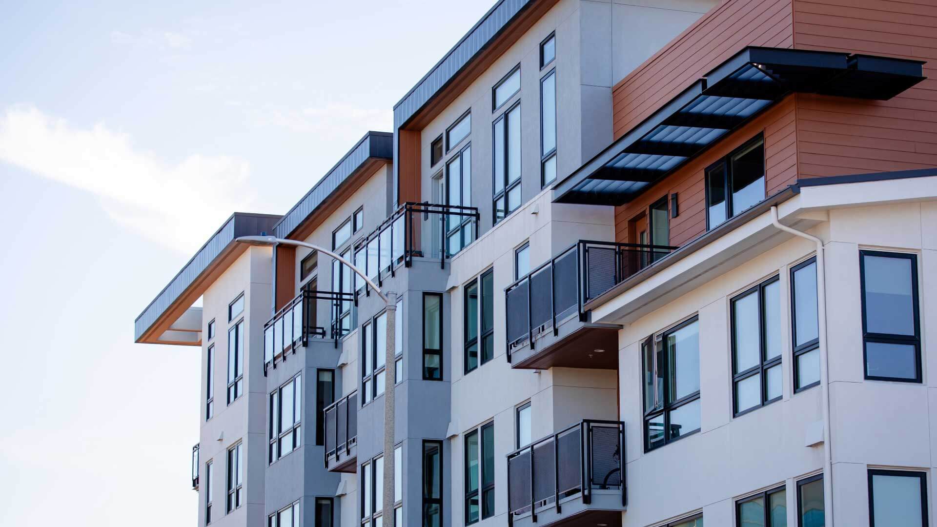 Modern apartment building featuring balconies and large windows, with a clear blue sky above.