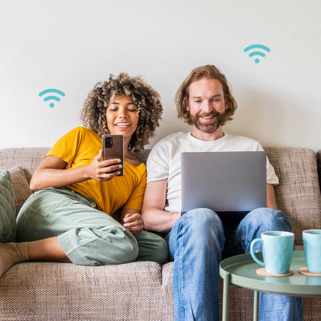 A woman and man sit on a couch, smiling while using a smartphone and laptop, with Wi-Fi icons above them.