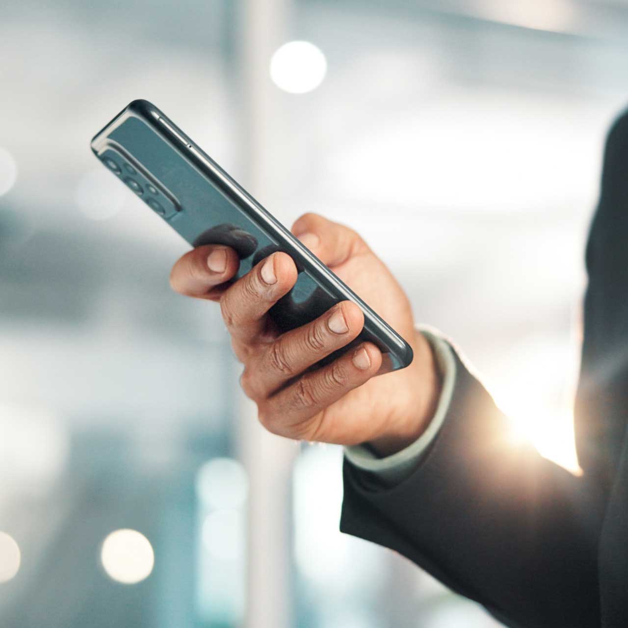 A close-up of a hand holding a smartphone, wearing a business suit with a blurred background.
