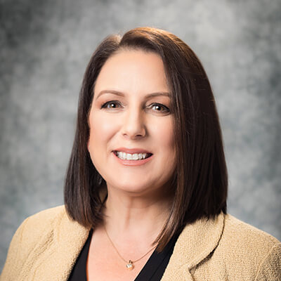 Professional headshot of a woman with shoulder-length brown hair, smiling against a gray backdrop.