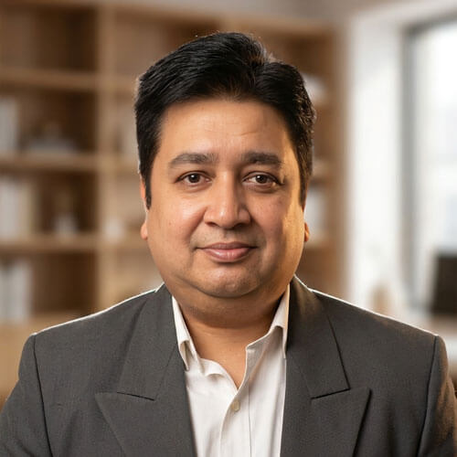 Professional headshot of a man in a gray suit, smiling in a modern office setting.